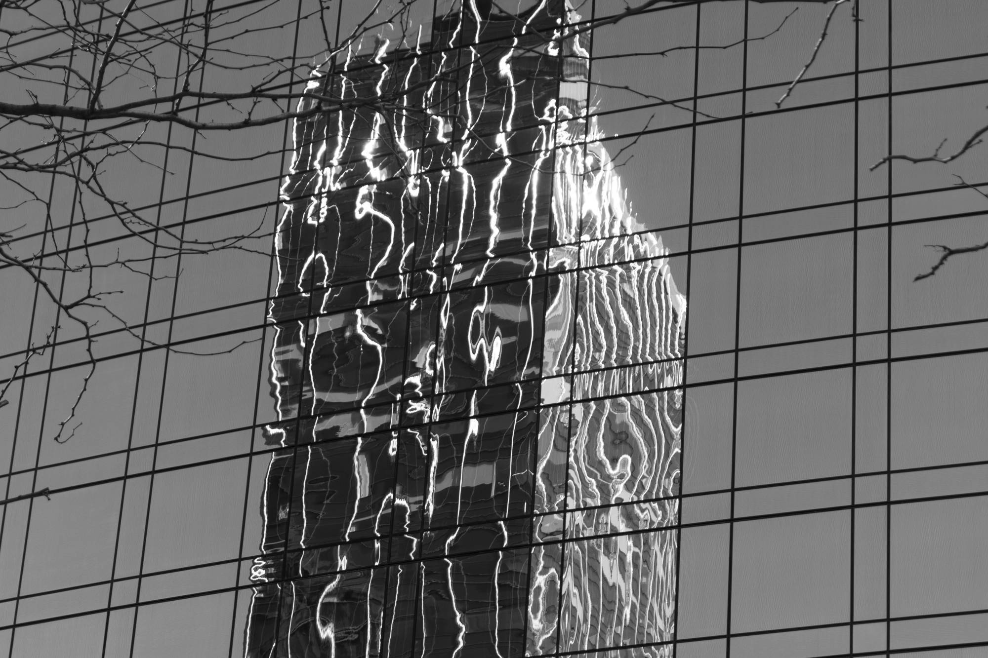 Black and white photograph of the reflection of a building in the windows of another building.